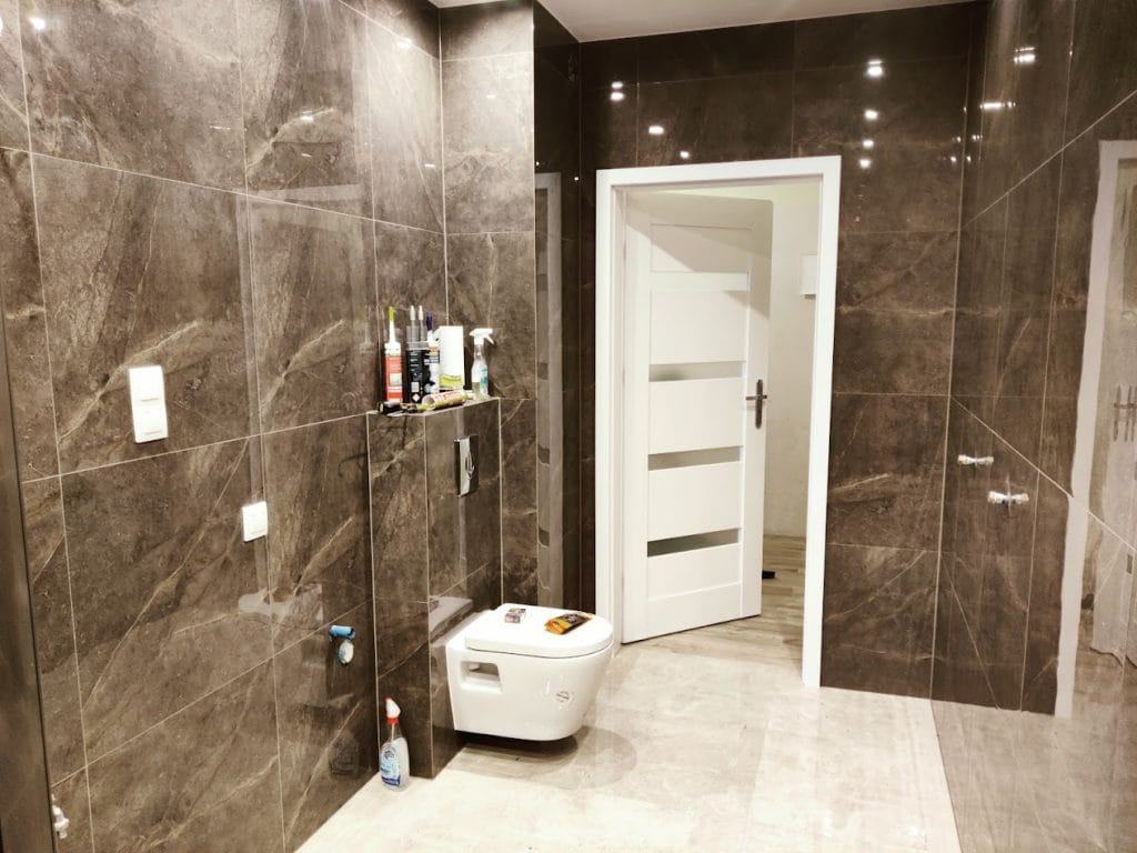 Nowoczesna łazienka w stylu glamour: ciemne, błyszczące ściany z gresu imitującego kamień skontrastowane z jasną podłogą i białą ceramiką sanitarną.